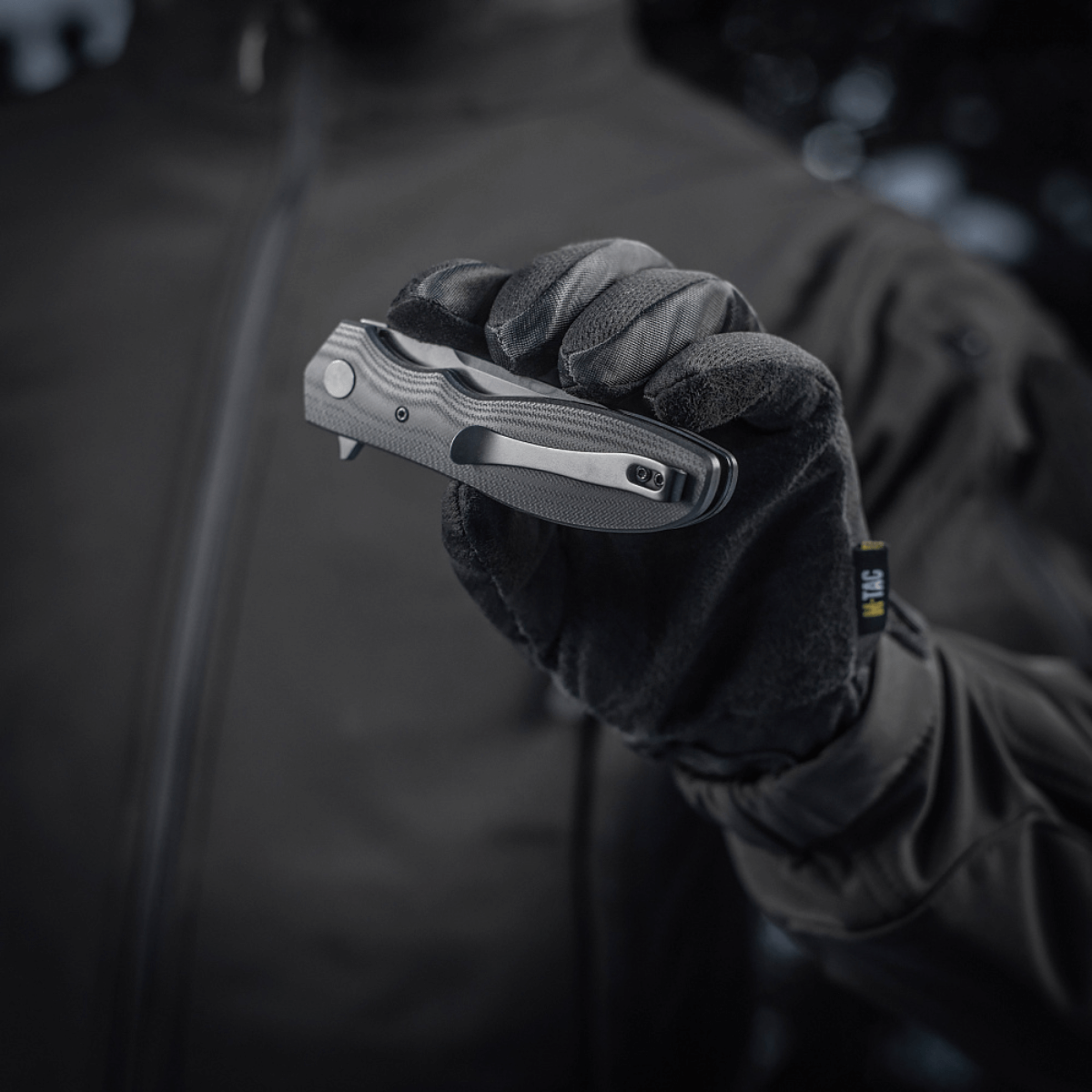 Henkilö käsineessä pitelee M-Tac Outdoor & Militær Type 6 -taittoveistä, musta G10-komposiittikahva.