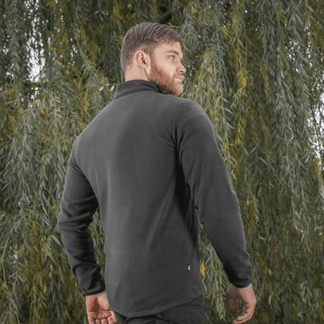 M-Tac Delta Polartec fleece-takki mustana nähtynä takaa miehellä vihreiden puiden taustaa vasten, sopii kylmiin päiviin.