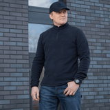 Mies pukeutuneena M-Tac Delta Polartec -fleece-takkiin muuriseinän edessä.