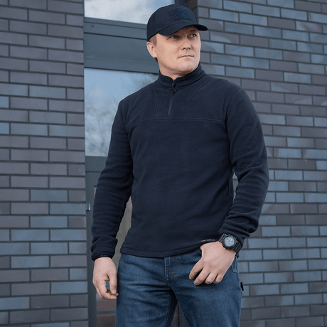 Mies pukeutuneena M-Tac Delta Polartec -fleece-takkiin muuriseinän edessä.