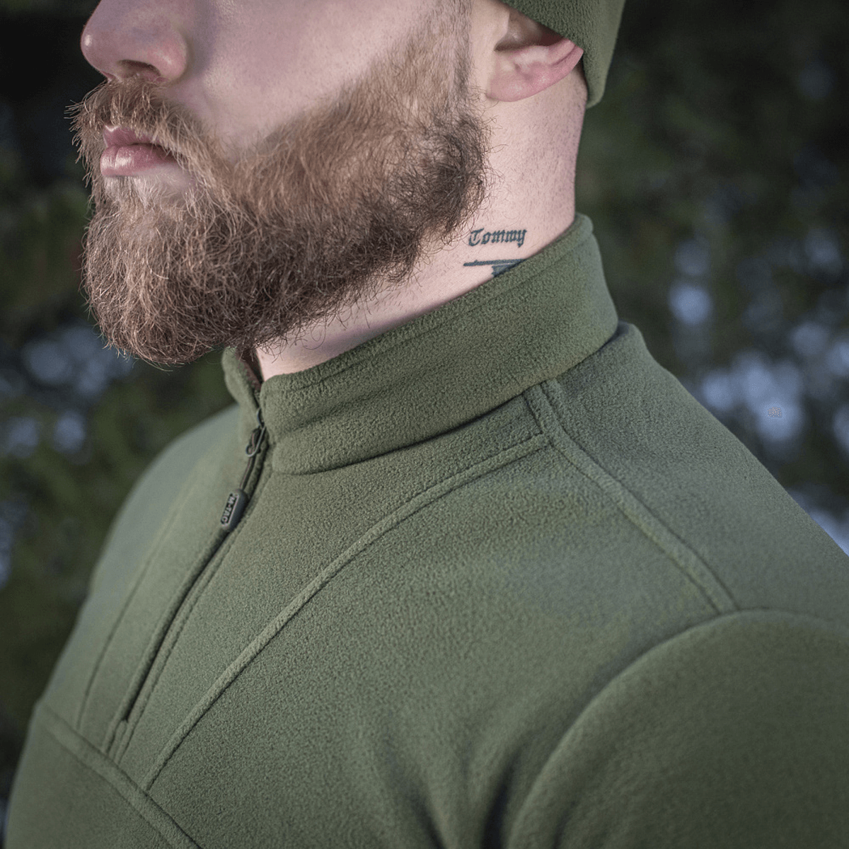 Mies pukeutuneena M-Tac Delta Polartec fleece-takkiin vihreänä, tatuointi kaulassa, sivuprofiili ulkoilmassa.