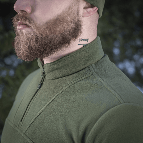 Mies pukeutuneena M-Tac Delta Polartec fleece-takkiin vihreänä, tatuointi kaulassa, sivuprofiili ulkoilmassa.