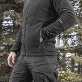 Mies pukeutuneena M-Tac Polartec Sport -fleecatakkiin metsässä, toimii lämpimänä ja toiminnallisena välikerroksena viileään säähän.