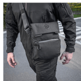 Mies kantaa M-Tac Konvert Taske Eliteä mustana, säädettävä olkahihna, Cordura 500D ja Cordura Hex 1000D.