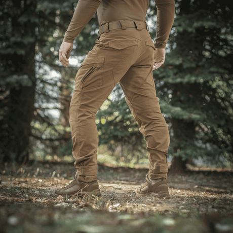 Henkilö metsässä pukeutuneena M-Tac Aggressor Gen.II Vintage -housuihin vintage-viimeistelyllä, sopivat peltoon ja arkeen.