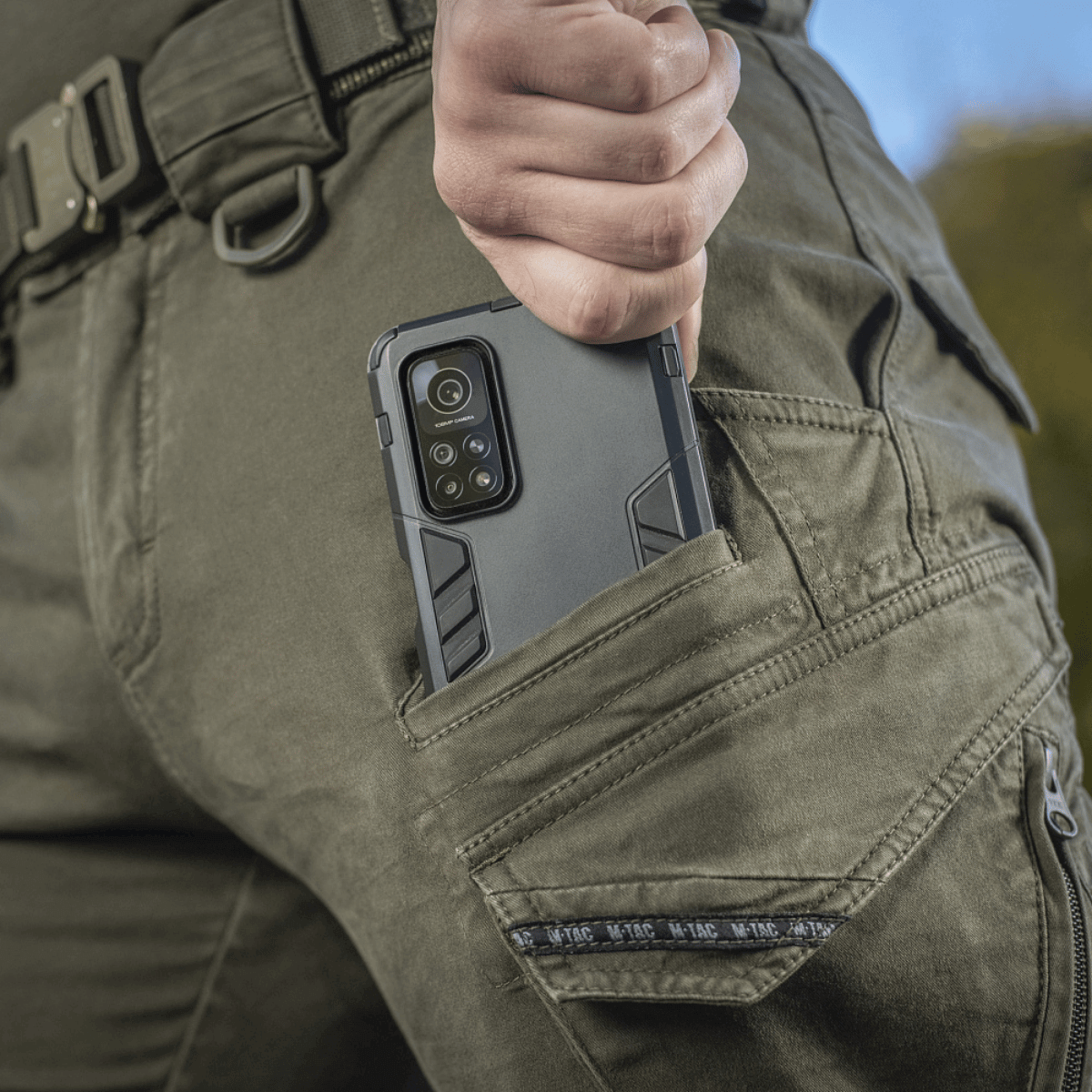 Lähikuva M-Tac Aggressor Gen.II Vintage -housuista, puhelin taskussa, näyttää käytännöllisen ja tyylikkään designin arkeen ja kentälle.