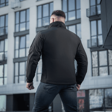 M-Tac Soft Shell -takki vesihylkivällä kalvolla ja fleece-vuorella, takaa kuvattuna modernia rakennusta vasten.