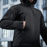 M-Tac Soft Shell -takki kaupunkiympäristössä, näyttää toiminnallisen takin vetoketjuilla ja taskuilla, sopii huonoon säähän.