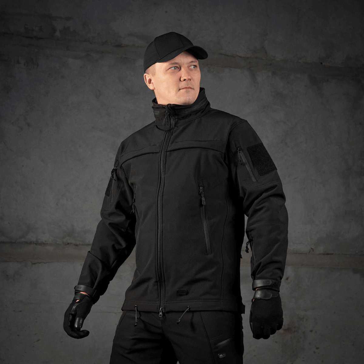 Mies pukeutuneena M-Tac Soft Shell Police Jakkeen valmis toimintaan, suojattuna tuulelta ja siltä säältä säädettävän hupun kanssa.