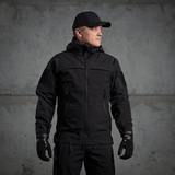Mies pukeutuneena M-Tac Soft Shell Police Jakkeen, musta takki säädettävin yksityiskohdin ja sisäinen fleece, suunniteltu tuulta ja säätä vastaan.