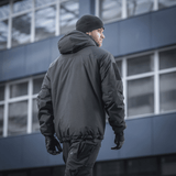 M-Tac Alpha Gen.III Pro -talvitakki, musta, takaa kuvattuna miehellä kaupungissa, suunniteltu äärimmäiseen kylmään ja sateeseen, parannettu G-Loft-täytteellä.