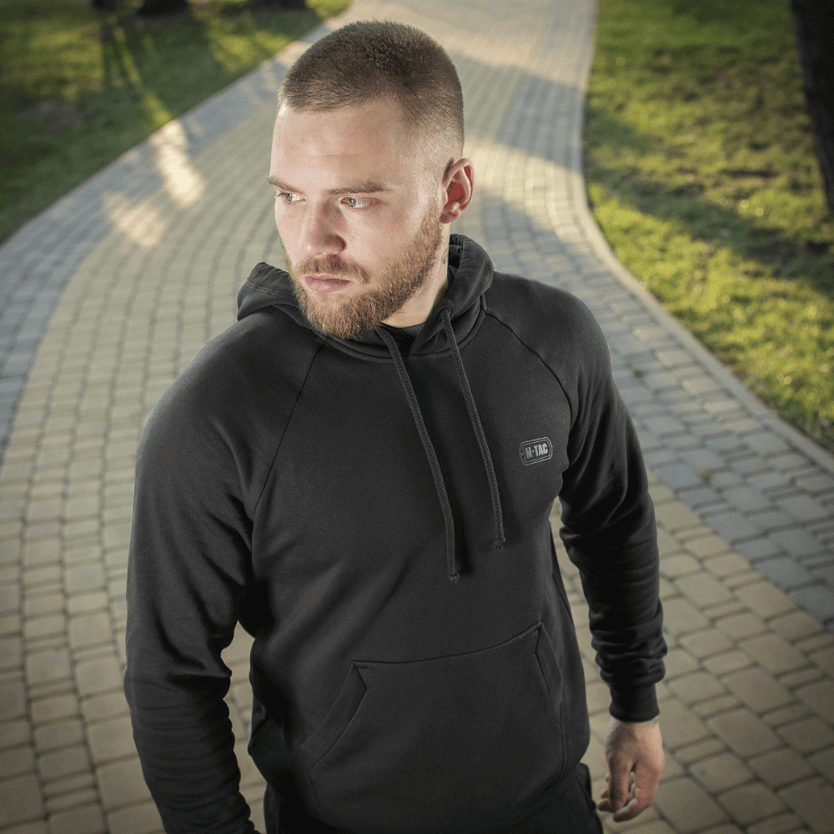 Mies M-Tac Cotton Raglan -hupparissa polulla vihreässä puistossa, mukava arki- ja urheiluvaate, 100 % puuvillaa.