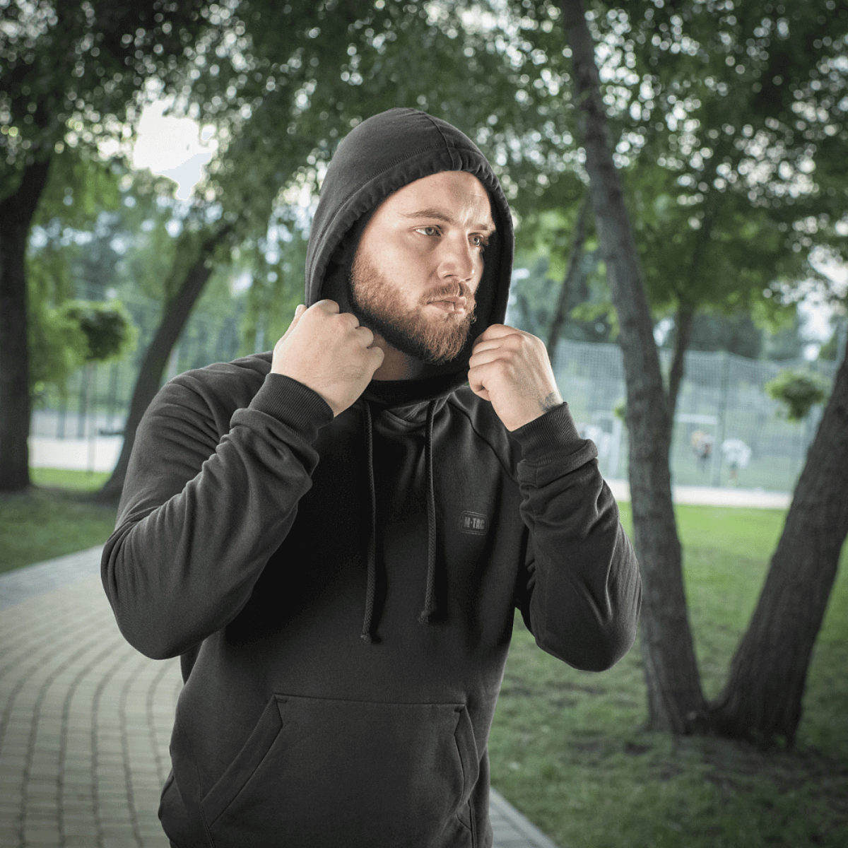 Mies mustassa M-Tac Cotton Raglan -hupparissa puistossa, valmis aktiviteetteihin.