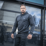 Mies M-Tac Cotton Raglan -hupparissa lasirakennuksen edessä, rennon ja mukavan näköinen, sopii arkeen.