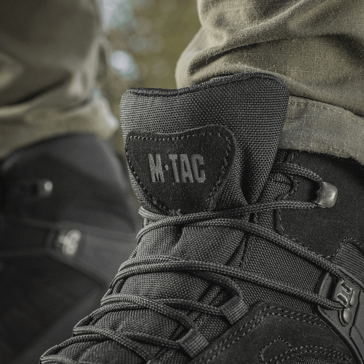 M-Tac Taktiske Sæsonstøvler mustasta nahasta ulkokäyttöön, lähikuva nauhoista ja logosta.