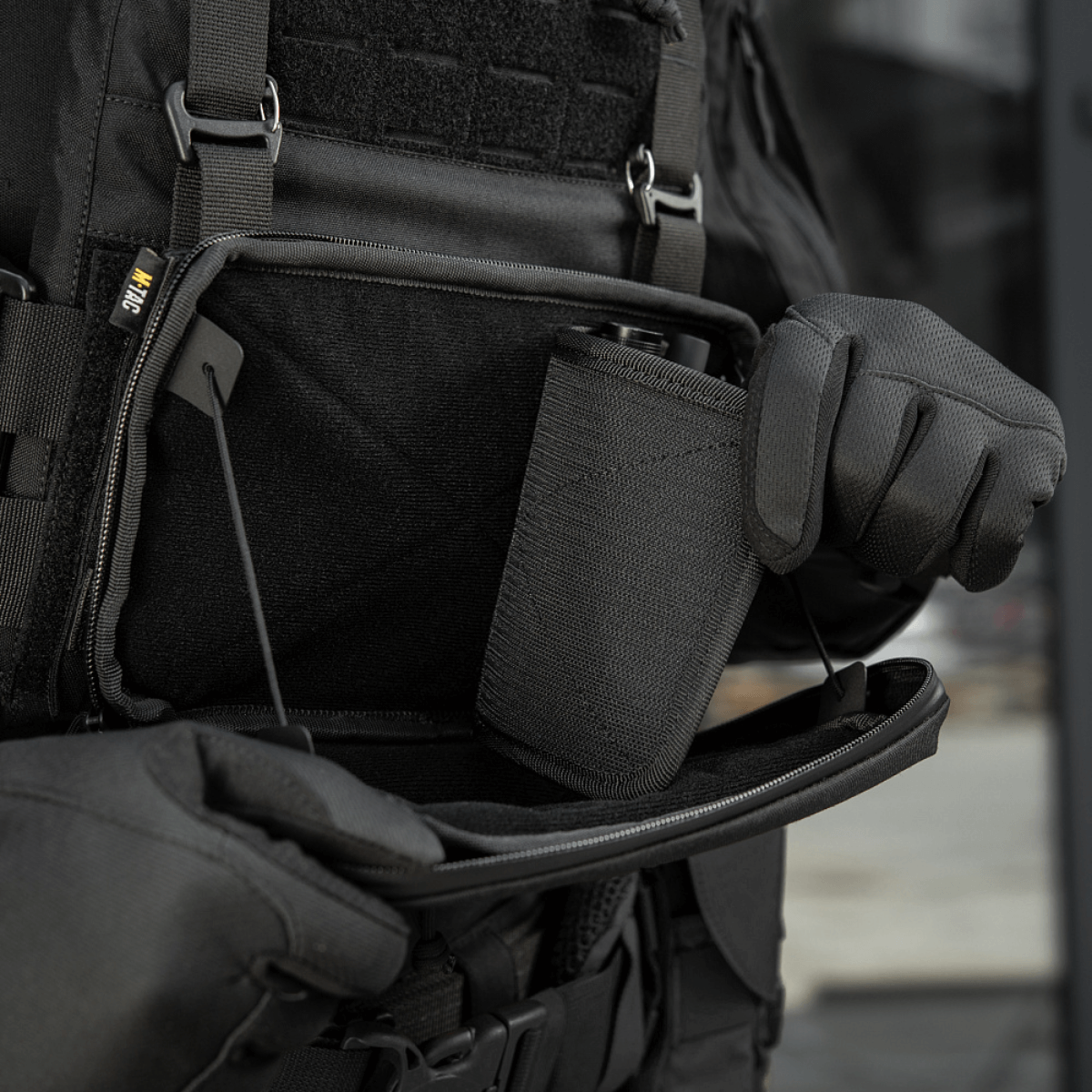 Henkilö avaa M-Tac Admin Pouch Large Elite Gen.II:n, jossa suuri säilytystila varusteille; valmistettu Cordura 500D:stä.