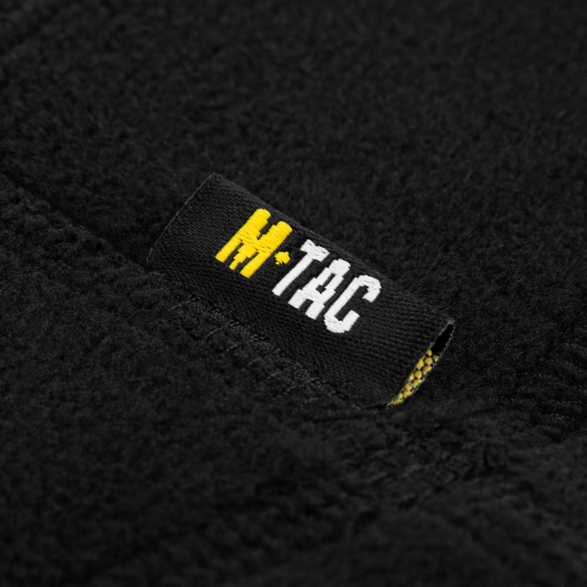 M-Tac Anatomisk Snood Justerbar Elite Fleece (320 g/m²) yksityiskohta merkistä mustassa fleece-materiaalissa.