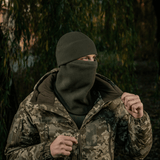 M-Tac Anatomisk Snood Justerbar Elite Fleece (320 g/m²) pidetään balaclavana kylmässä säässä, taustalla metsä ja maastokuvioinen takki.