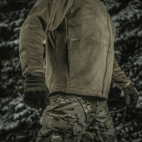 Sotilas pukeutuneena M-Tac Battle Fleece Polartec -takkiin metsässä, näyttää takin toiminnallisuuden ja istuvuuden.