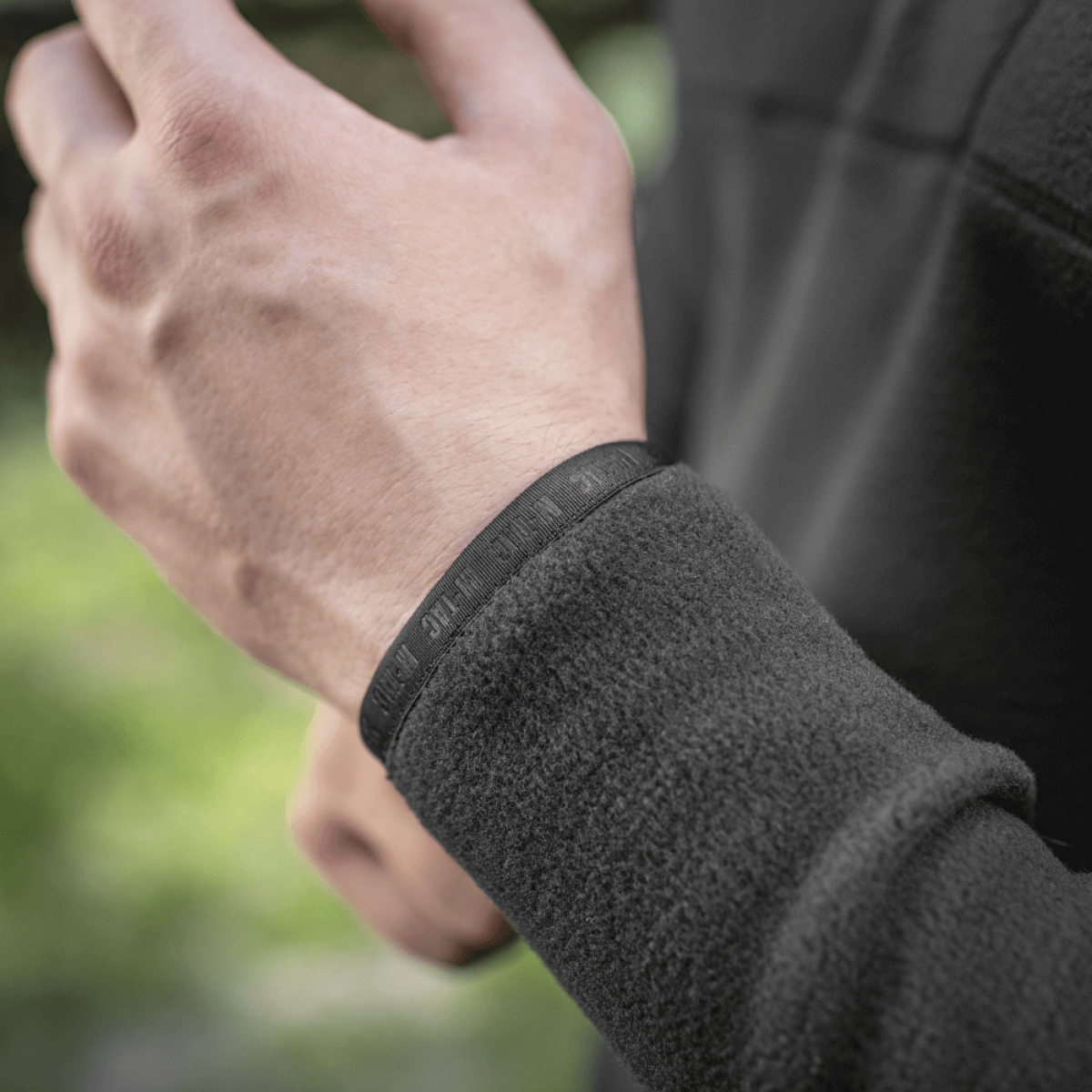 Mies pukeutuneena M-Tac Delta Polartec Raglan -takkiin, näyttää fleece-yksityiskohdan ja joustavan nauhan, soveltuu ulkoiluun.