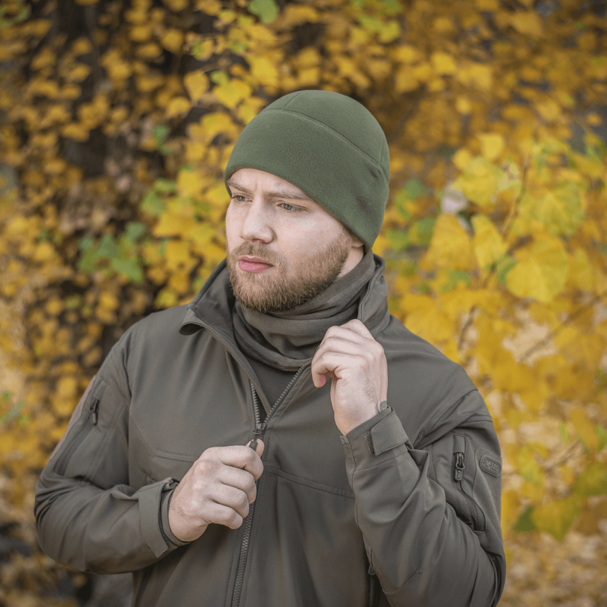 Mies pukeutuneena vihreään M-Tac Fleece Polartec Watch Cap -pipoon syksymaisemassa, sopii ulkoiluun viileissä ja kylmissä olosuhteissa.