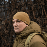 Mies pukeutuneena M-Tac Fleece Watch Cap Light Polartec hattuun ruskeissa sävyissä, sopii suojaksi kylmältä ja tuulelta.