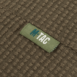 Lähikuva M-Tac Hjelm Watch Cap Polartec -tekstiilirakenteesta M-Tac-logolla, ihanteellinen kylmään säähän ja mukavuutta kypärän alla.