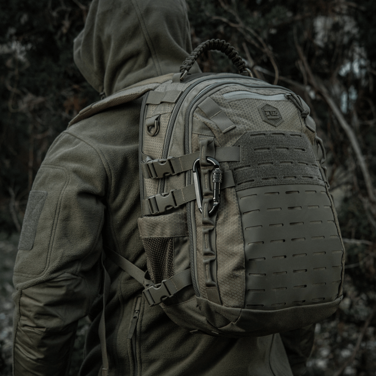 Reppu, jossa M-Tac karabiinihaka 10 cm sotavarusteissa, valmistettu 40Cr-seosteräksestä, esitetty metsäympäristössä.