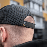 Miehellä on M-Tac Mesh Flex Ripstop Baseball Cap säädettävällä Velcro-nauhalla ja mesh-paneelilla ilmanvaihtoon ulkoilmassa.