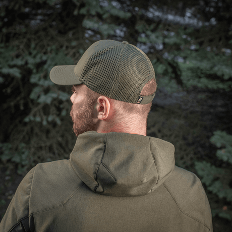 Mies metsässä käyttää M-Tac Mesh Flex Ripstop Baseball Capia; näkyvillä mesh-paneelit ja Velcro-tarranauha. Sopii ulkoaktiviteetteihin.