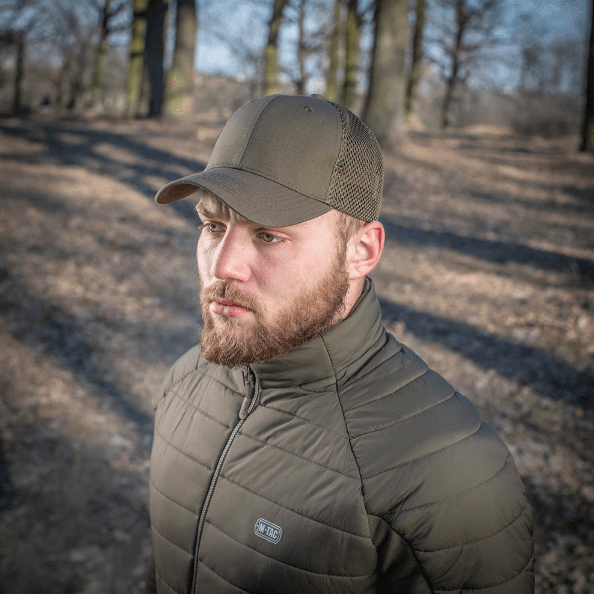 Mies metsässä, M-Tac Mesh Flex Ripstop Baseball Cap en, jossa näkyvät mesh-paneelit ja kestävä muotoilu ulkokäyttöön.