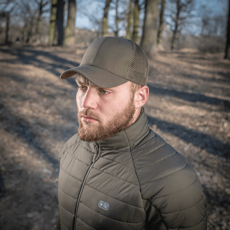 Mies metsässä, M-Tac Mesh Flex Ripstop Baseball Cap en, jossa näkyvät mesh-paneelit ja kestävä muotoilu ulkokäyttöön.