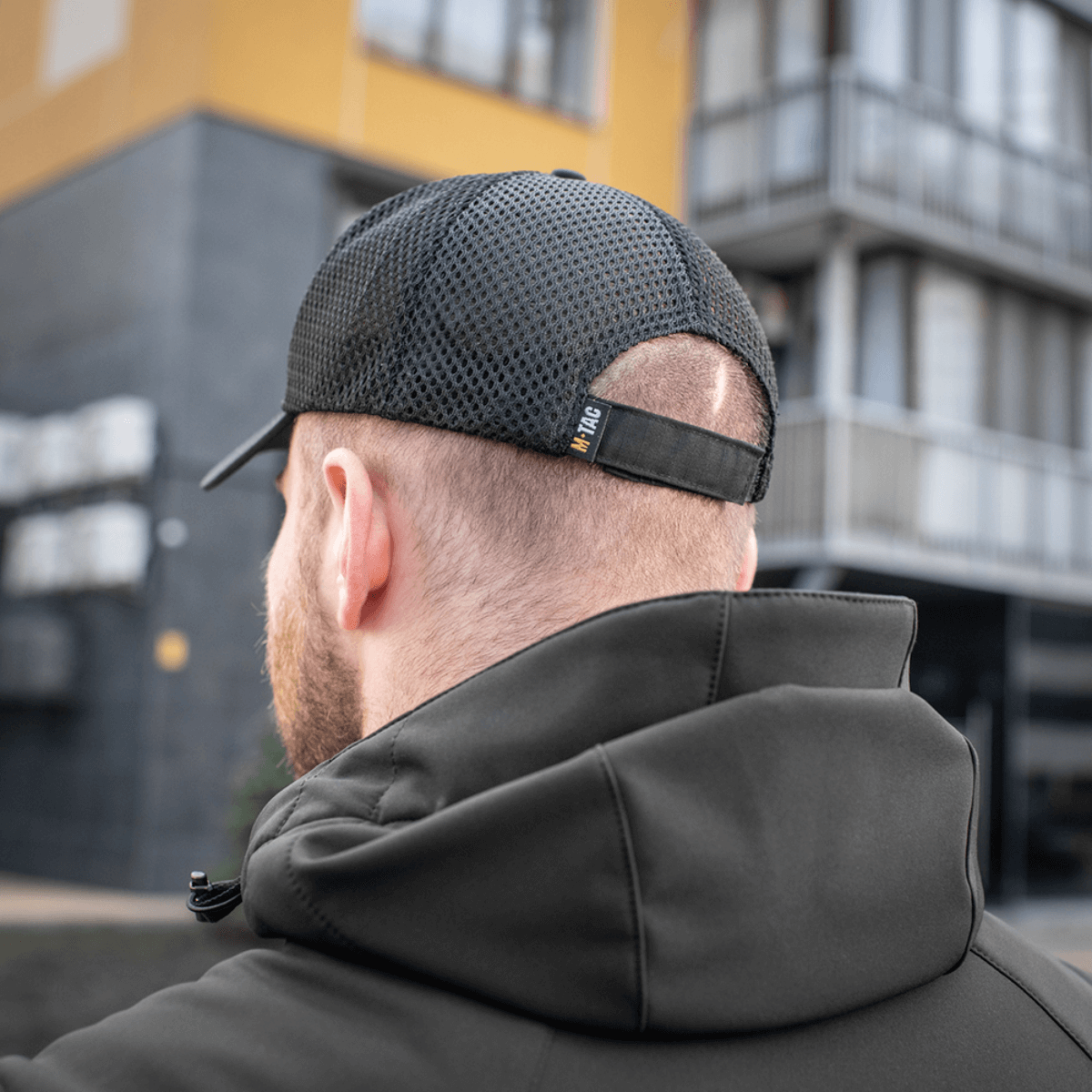 M-Tac Mesh Flex Ripstop Baseball Cap meshistä nähtynä takaa, en henkilö mustassa takissa, näkyy säädettävä Velcro-strop.