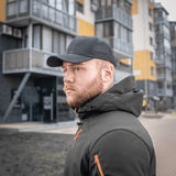 Mies mustassa M-Tac Mesh Flex Ripstop Baseball Cap en kaupungin edessä, kuva näyttää ulkoiluun liittyvää kestävyyttä ja tyyliä.