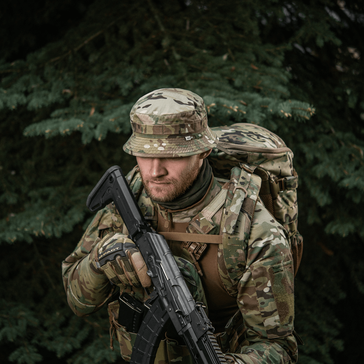 Mies maastoverkossa M-Tac Panama Hat Gen.II NYCO päässään, taktinen univormu ja reppu metsäympäristössä.