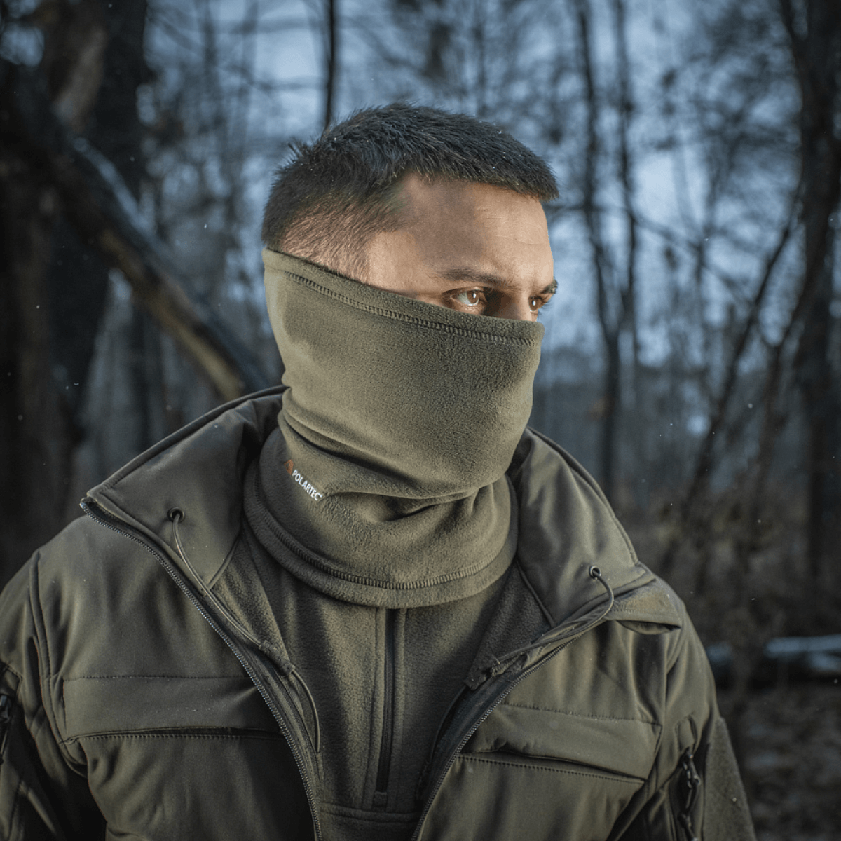 Mies käyttää M-Tac Tube Scarf Polartec -tuubia kasvomaskina metsässä, suojaa kylmältä ja tuulelta ulkoillessa.