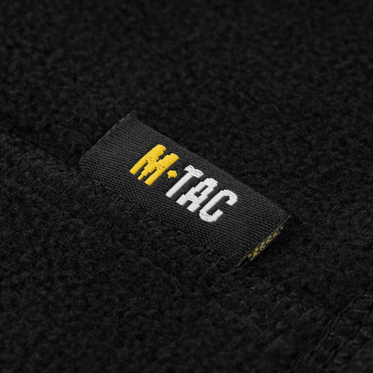 M-Tac Snood Elite Kort Justerbar Fleece -etiketti mustassa fleecessä, osoittaa kestävän ja pehmeän materiaalin, ihanteellinen kylmään säähän.