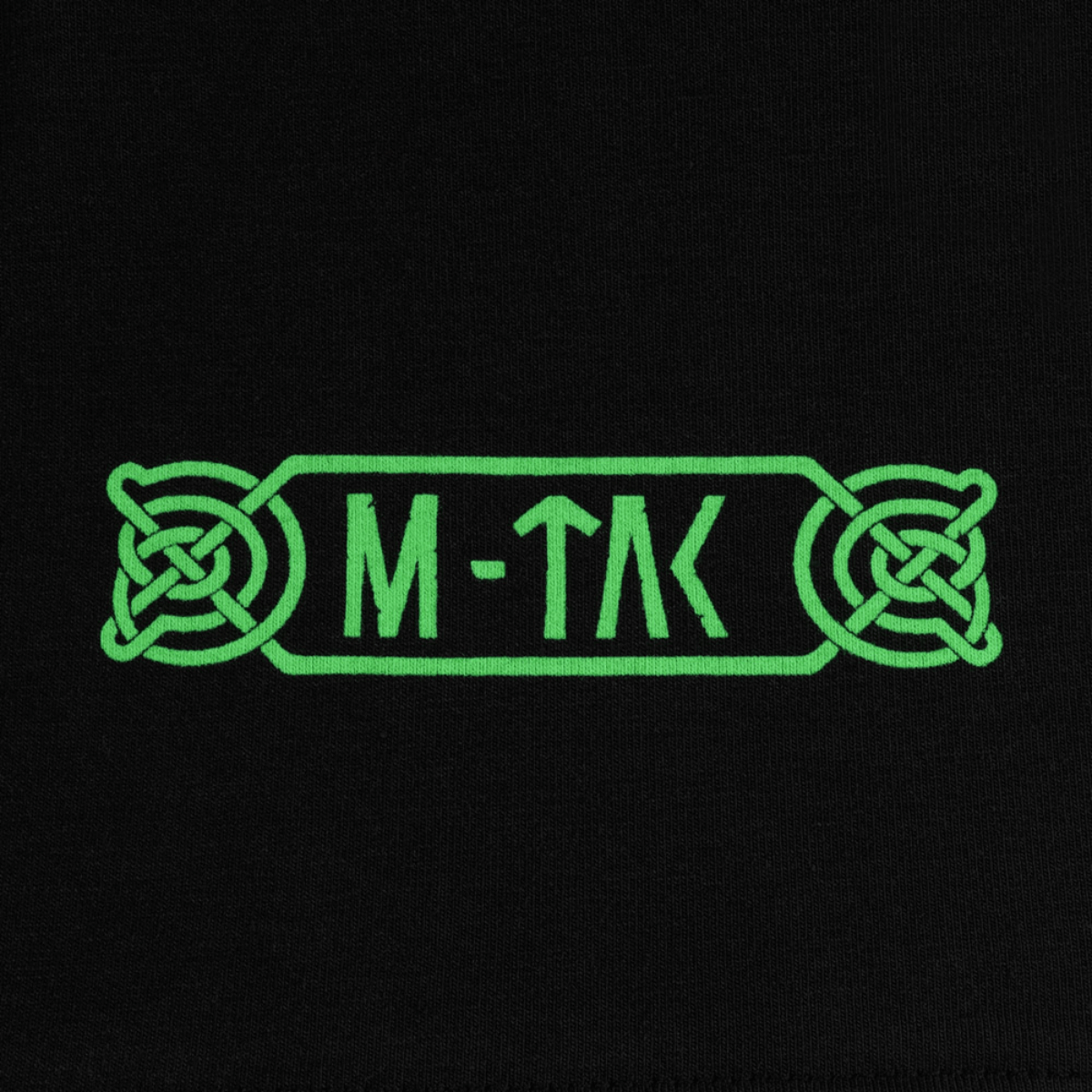 Lähikuva M-Tac T-Shirt Night Vision -logosta vihreässä pohjoismaisessa tyylissä, Odinin mytologiasta inspiroituna, mustalla taustalla.