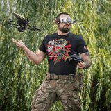 Mies pukeutuneena M-Tac T-Shirt Kamikaze Spirit -paitaan, FPV-lasit ja drone metsäympäristössä.
