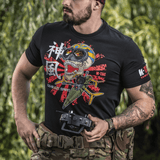 Mies pukeutuneena M-Tac T-Shirt Kamikaze Spirit -paitaan, jossa tyylitelty kallokuvio ja FPV-goggles, seisoo ulkona ohjain kädessä.