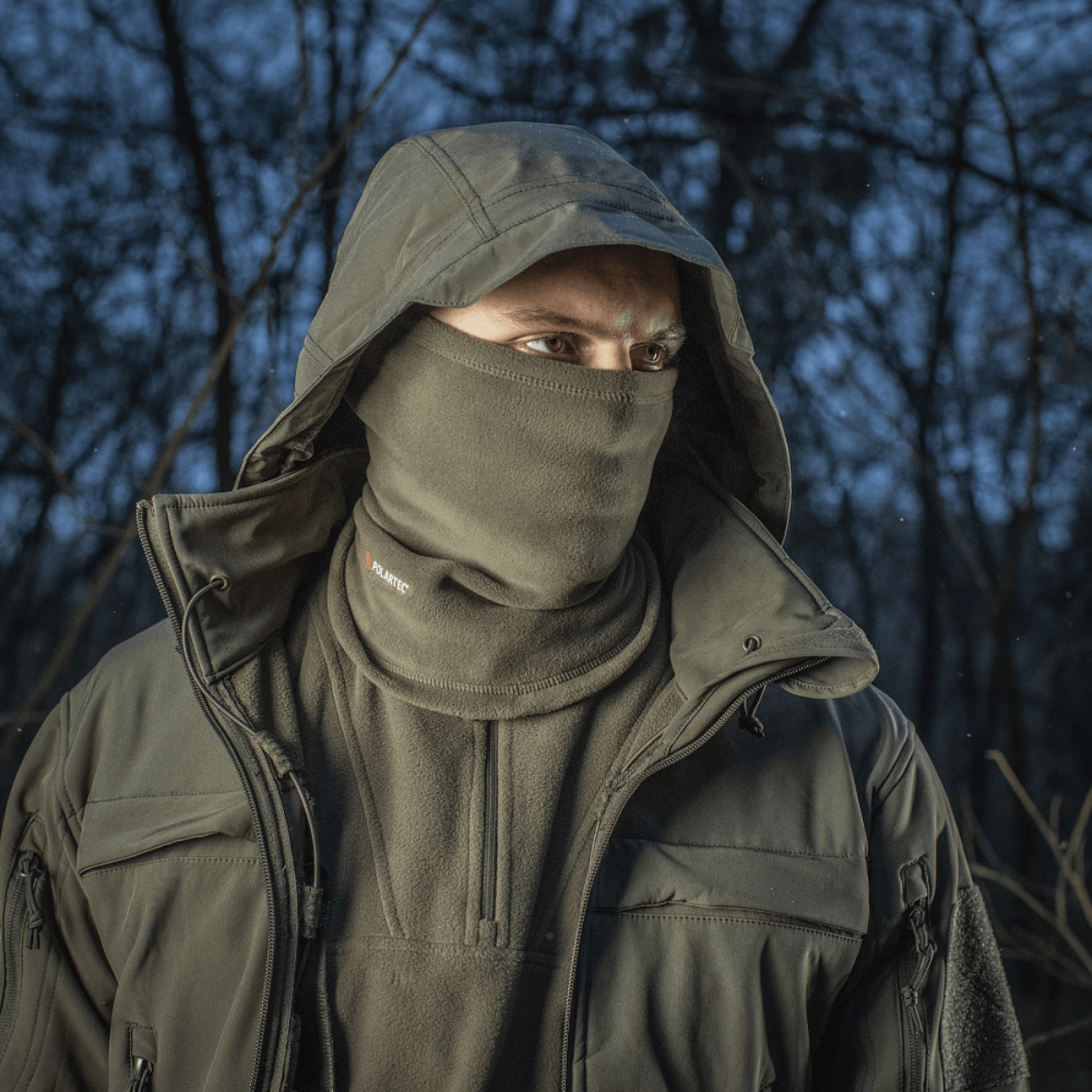 Mies metsässä käyttäen M-Tac Tube Scarf Polartec -kauluria, suoja säätä vastaan Polartec Micro Series fleece -materiaalista, ulkoilutyyli.