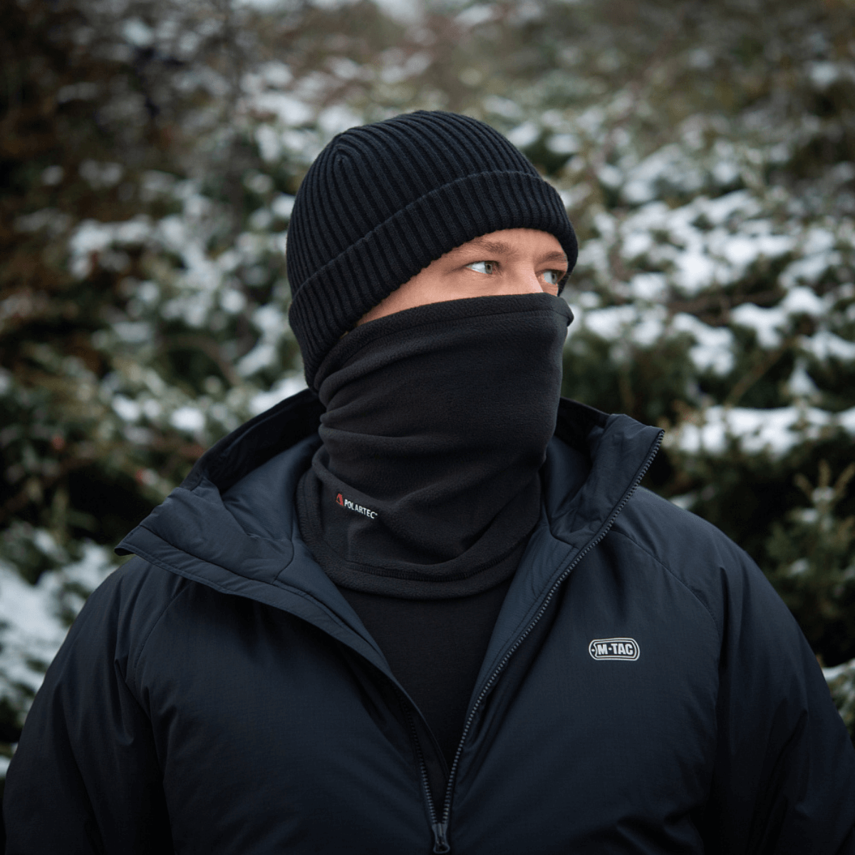 Mies käyttää M-Tac Tube Scarf Polartec -kauluria lumisessa maisemassa, suojaten kylmältä yhdessä takin kanssa.