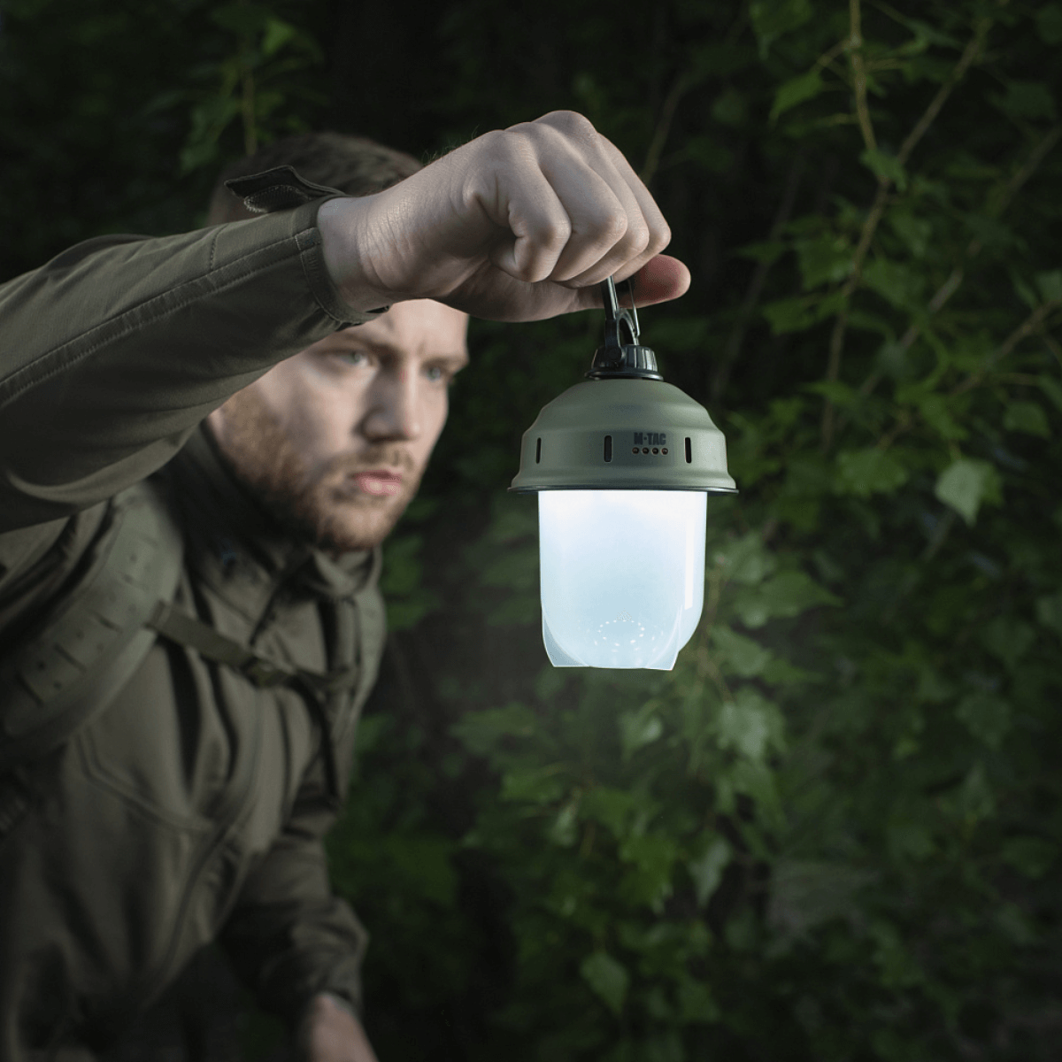 Mies pitää M-Tac retkeilyriippuvalaisinta metsässä, ihanteellinen retkeilyyn, kalastukseen ja metsästykseen 200 lumenin LED-valolla.