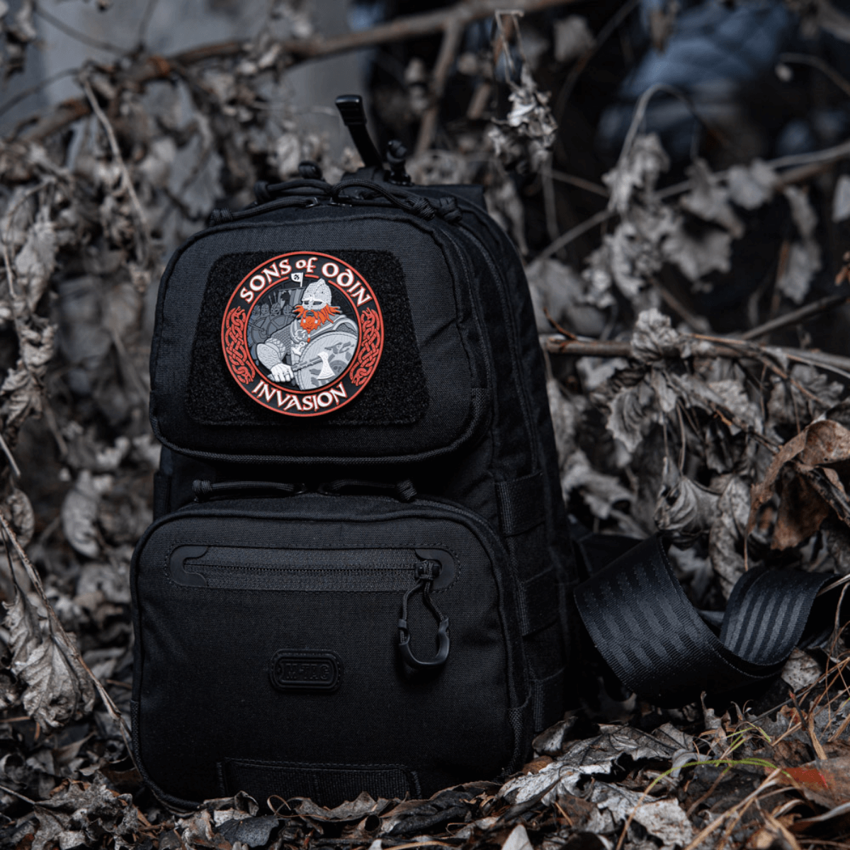 Musta reppu, jossa M-Tac Patch Sons of Odin 3D Velcro metsäympäristössä, sopii taktiseen käyttöön ja vapaa-aikaan