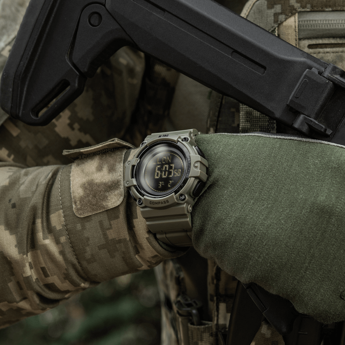 M-Tac Tactical Ur med Kompas 2233 käytössä ulkoilma-taktiikkatilanteessa, korostaa kestävyyttä ja toimintoja kuten kompassi ja LED-taustavalo.