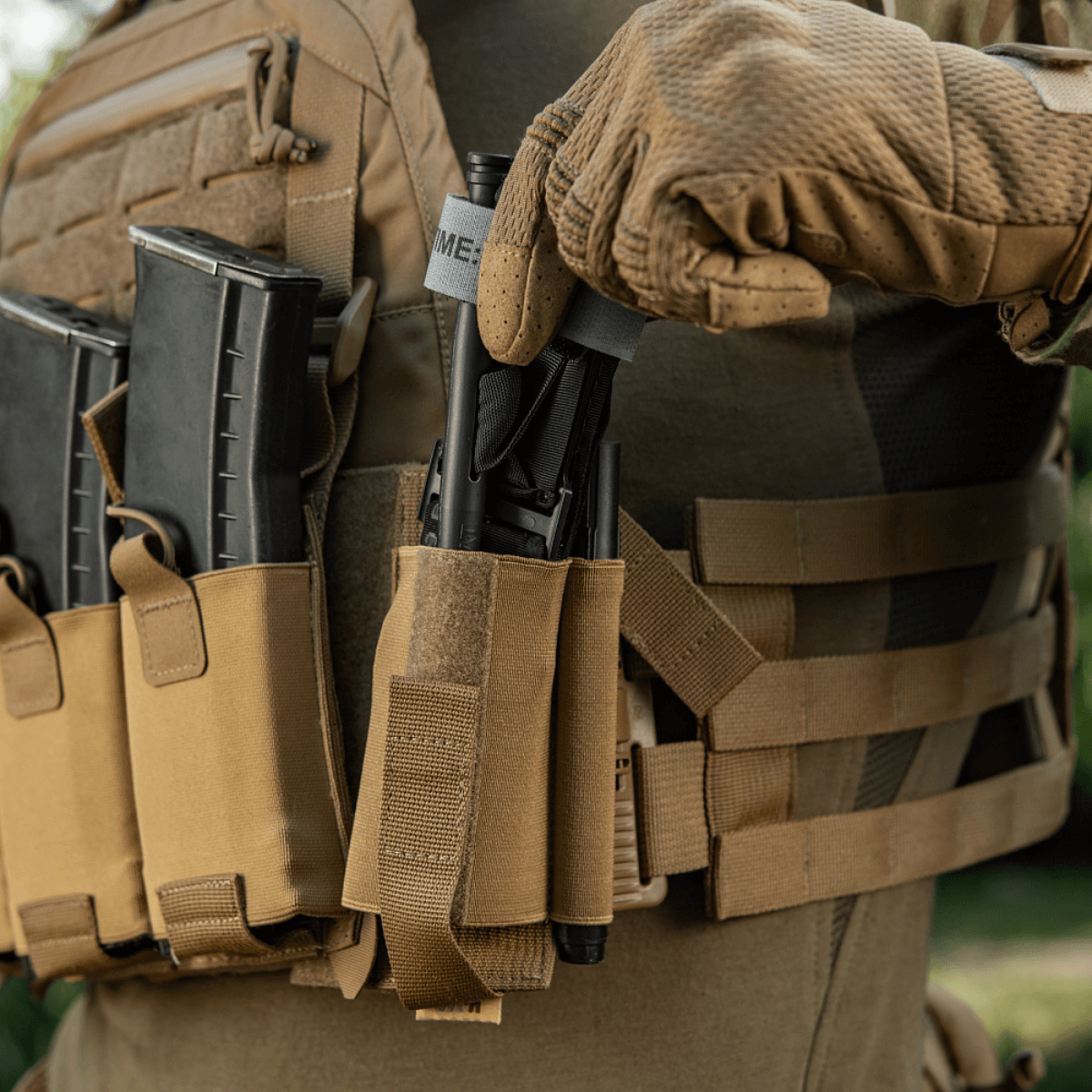 Henkilö taktisen liivin kanssa, M‑Tac Tourniquet Pouch Elastic Gen.5, Coyote Brown, CAT-tourniquetin säilytykseen.