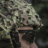 M‑Tac Vilha Hjelmcover Elite Multicam-camossa henkilöllä, valmiina suojaamaan kypärää likaa ja kulumista vastaan haastavissa olosuhteissa.