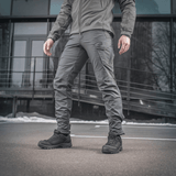 Mies pukeutuneena M-Tac taktisiin housuihin Aggressor Gen. II Flex; sopivat harjoitteluun, ampumiseen, työhön ja vapaa-aikaan, rip-stop-kangas ja Teflon-pinnoite