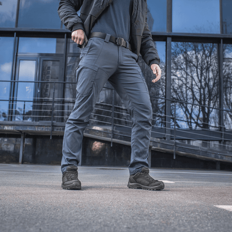 Mies pukeutuneena M-Tac housuihin Sahara Flex Light modernin rakennuksen edessä, korostaen housujen joustavuutta ja tyylikästä designia.