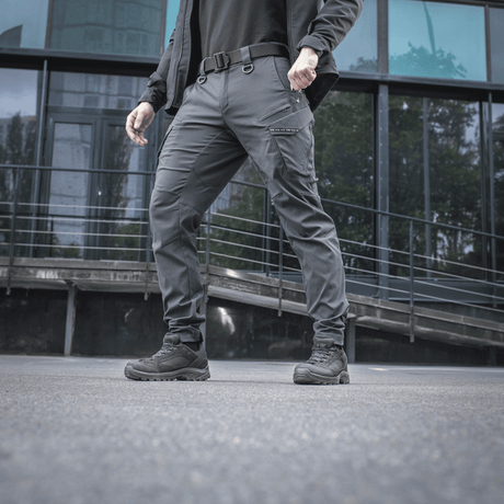 Mies pukeutuneena M-Tac-housuihin Aggressor Summer Flex modernin rakennuksen edessä, näyttää kevyen Rip-Stop-nylonin.